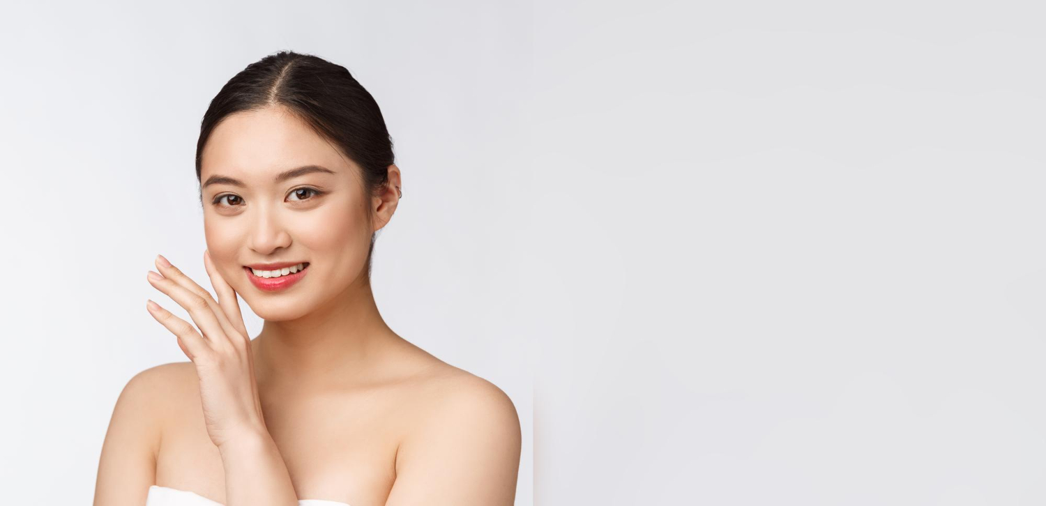 Smiling woman with dark hair in a neat bun, touching her cheek against a white backdrop.