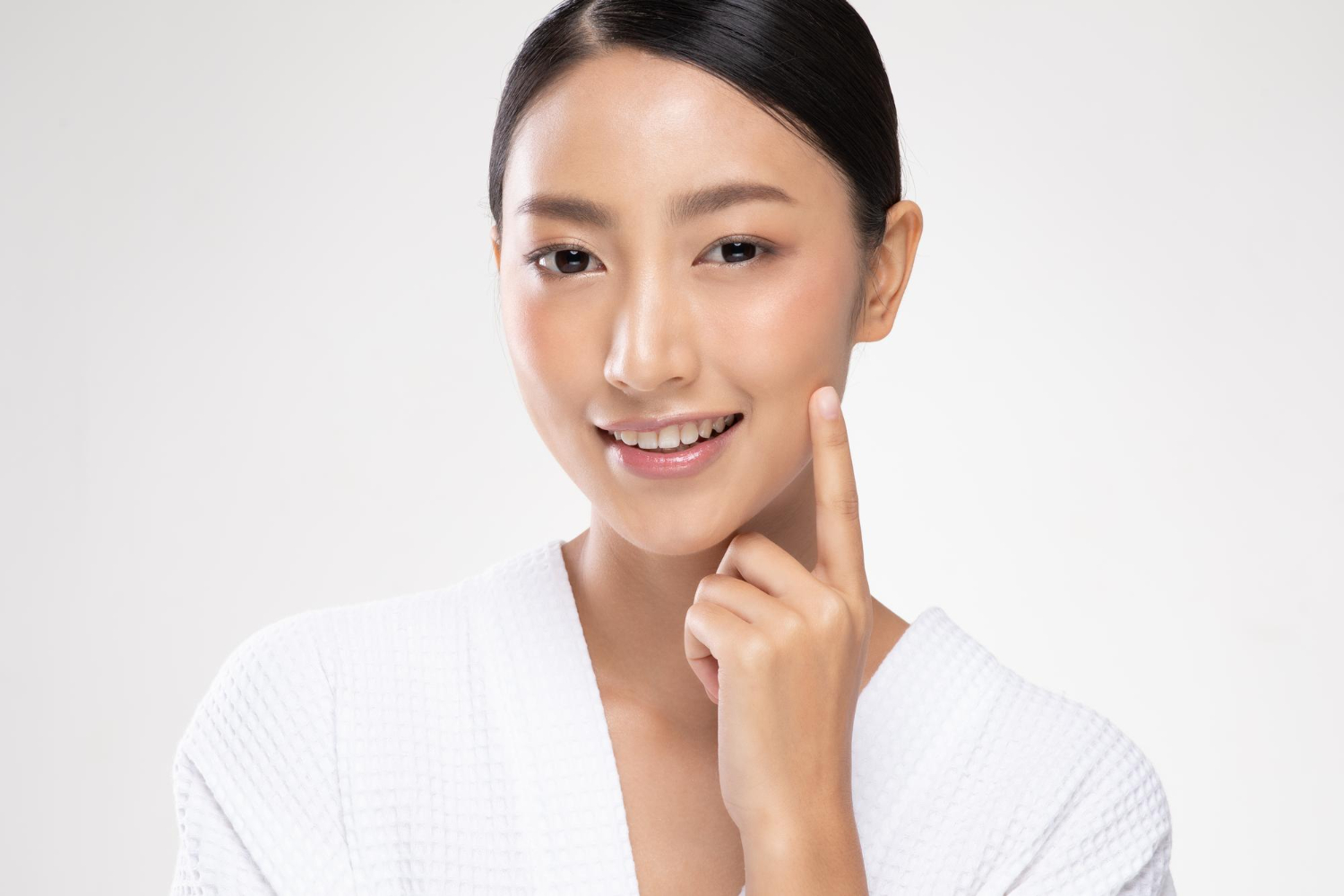 Smiling Asian woman in a white robe touching her cheek with her index finger