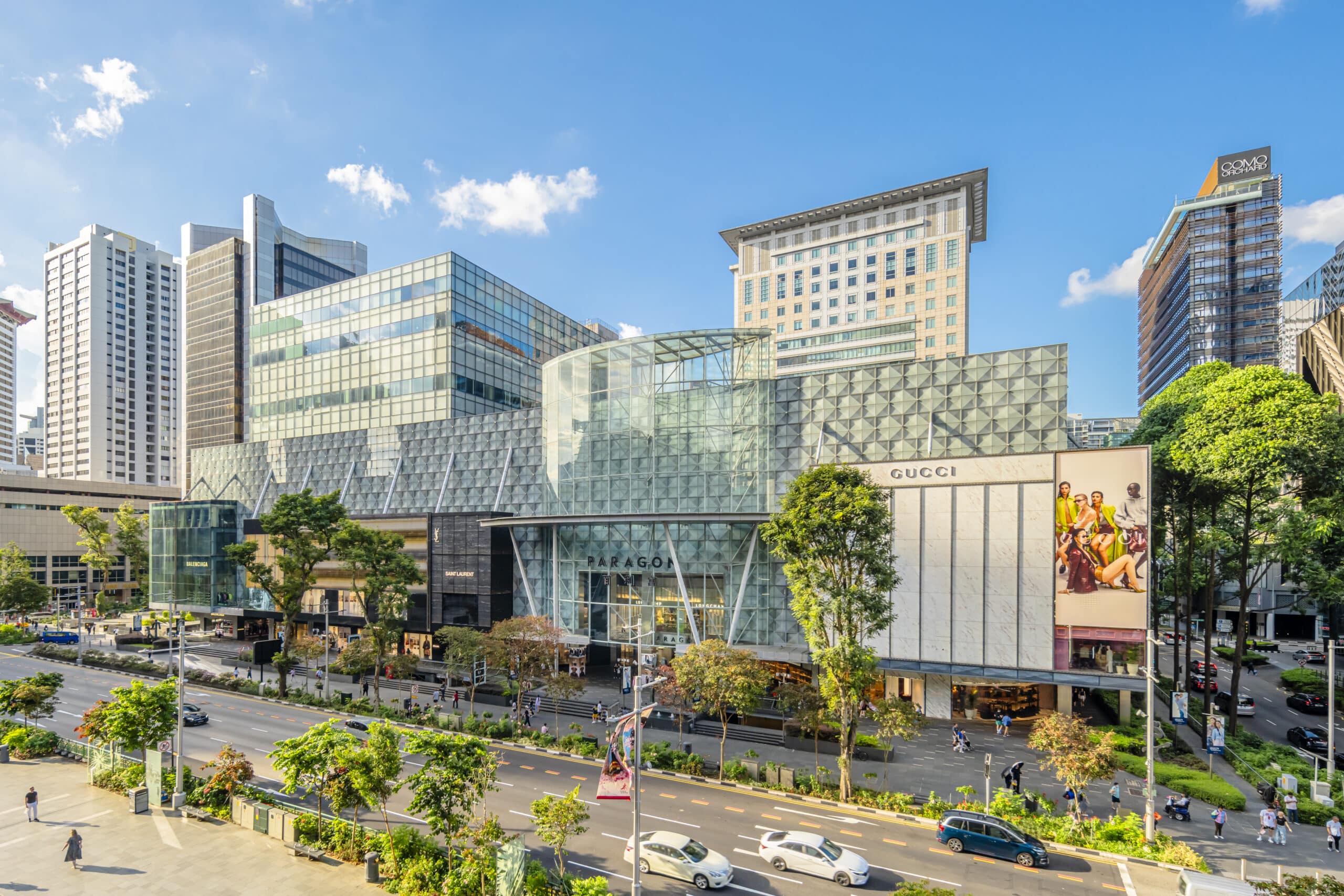 Modern shopping mall with glass facade and Gucci storefront; busy city street in foreground.