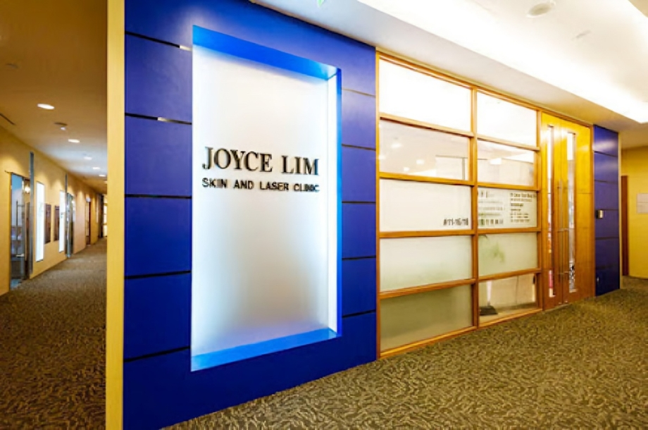 Indoor hallway outside Joyce Lim Skin and Laser Clinic, with a blue-framed frosted sign displaying the clinic name against a blue wall paneling.